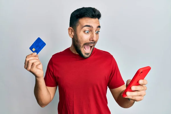 Joven Hombre Hispano Sosteniendo Teléfono Inteligente Tarjeta Crédito Celebrando Loco —  Fotos de Stock