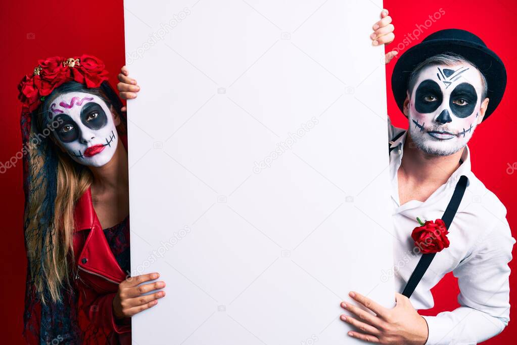 Couple wearing day of the dead costume holding blank empty banner thinking attitude and sober expression looking self confident 