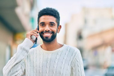 Genç Afrikalı Amerikalı gülümseyen mutlu bir adam şehirdeki akıllı telefondan konuşuyor..