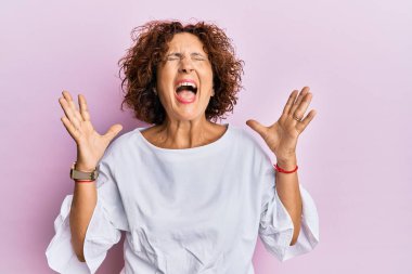 Güzel, orta yaşlı olgun bir kadın pembe arka plan üzerine zarif kıyafetler giyip kollarını kaldırmış ve gözleri kapalı heyecanlı bir şekilde başarıyı kutluyor. Kazanan konsept 