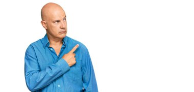 Orta yaşlı, kel bir adam, günlük giysiler giymiş, elini kaldırmış, ciddi ve sakin bir yüz ifadesi sergiliyor. 