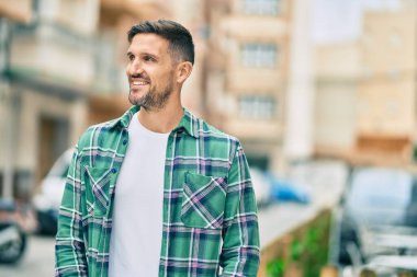 Genç beyaz adam gülümseyerek şehirde mutlu mesut duruyor..