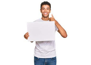Genç, yakışıklı, Afro-Amerikalı, elinde boş afiş tutan mutlu ve olumlu gülümseyen, başparmağını kaldırmış, mükemmel ve onay işareti yapan bir adam. 