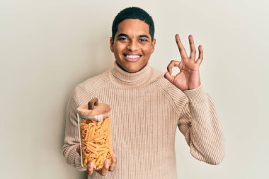 Genç, yakışıklı, elinde makarna kavanozu olan İspanyol bir adam parmaklarıyla imza atıyor, gülümseyerek mükemmel bir sembol oluşturuyor. 