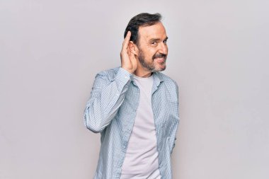 İzole edilmiş beyaz arka planda dikilen sıradan bir kot gömlek giyen yakışıklı bir adam kulağına fısıldayarak dedikodu ya da dedikoduları dinliyor. Sağırlık kavramı.