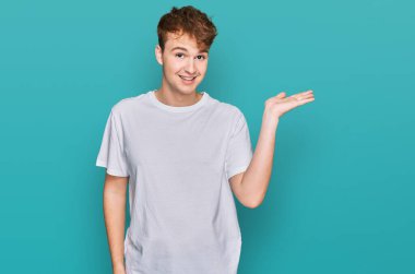 Beyaz günlük tişört giyen, neşeli gülümseyen, avuç içi dolu genç beyaz bir adam kameraya bakıyor.. 