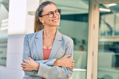 Sarışın iş kadını kollarını kavuşturup şehirde mutlu mesut gülümsüyor..