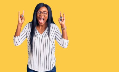 Sıradan kıyafetler ve gözlük takmış, çılgın bir ifadeyle bağıran, elleri havada rock sembolü yapan genç Afrikalı Amerikalı bir kadın. Müzik yıldızı. ağır müzik konsepti. 