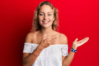Güzel, beyaz bir kadın, kırmızı arka plan üzerine gündelik giysiler giyip kameraya hayret ediyor ve gülümsüyor.. 