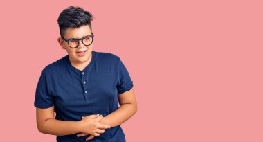 Küçük çocuk gündelik kıyafetler giyiyor ve elleri karnında gözlük takıyor çünkü mide bulantısı, acı verici bir hastalık kendini iyi hissetmiyor. Ağrı kavramı. 