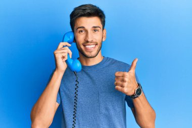 Klasik telefonda gülümseyen, mutlu ve olumlu gülümseyen, mükemmel ve onay işareti yapan genç yakışıklı adam. 