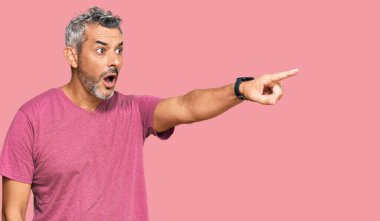 Orta yaşlı, gri saçlı, sıradan kıyafetler giyen, parmakları önde olan, ağzı açık, ağzı açık, şaşırmış bir adam. 