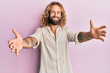 Sakallı, uzun saçlı, sıradan kıyafetler giyen yakışıklı bir adam kameraya sarılıp gülümsüyor. Mutluluğu kucaklayan neşeli bir ifade.. 