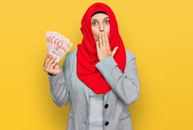 İslamcı başörtüsü takan güzel İspanyol kadın Singapur dolarları tutuyor. Ağzını elle kapatan banknotlar, şok olmuş ve hata yapmaktan korkuyor. şaşırmış ifade 