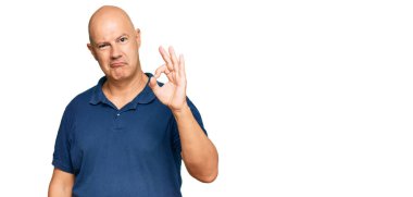 Orta yaşlı, kel, günlük kıyafetler giyen, gülümseyen, el ve parmaklarıyla imza atan bir adam. başarılı ifade. 