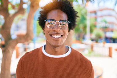Genç, yakışıklı, Afro-Amerikalı, günlük kıyafetler ve mutlu gülümseyen gözlükler takıyor. Yüzünde tebessümle dikilip kameraya bakıyor ve caddede yürüyor..