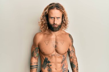 Handsome man with beard and long hair standing shirtless showing tattoos skeptic and nervous, frowning upset because of problem. negative person. 