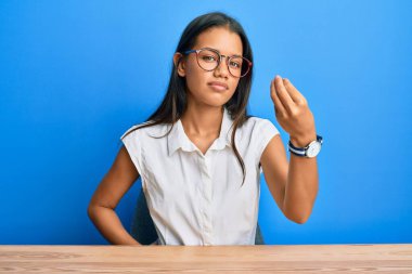 Güzel İspanyol kadın, gündelik giysiler içinde masaya oturmuş İtalyan jestleri yapıyor. Elleri ve parmakları kendinden emin bir ifadeyle. 