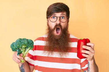 Uzun sakallı, elinde brokoli ve kırmızı biber olan yakışıklı genç adam şaşkınlık ve şaşkınlık ifadesi, korku ve heyecanlı yüz ifadesiyle dehşete düşmüş ve şok olmuştu.. 