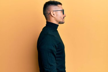 Balıkçı yaka kazak ve gözlük takan yakışıklı bir adam. Taraf arıyor, rahat profil pozu veriyor, doğal bir yüzü ve kendine güvenen bir gülümsemesi var.. 