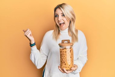 Genç beyaz kadın elinde makarna kavanozu tutarken başparmağıyla ağzını açıp gülümsüyor. 