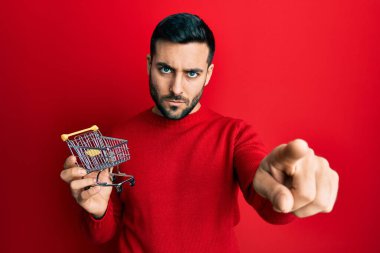 Elinde küçük bir süpermarket arabası olan genç İspanyol bir adam kamerayı işaret ediyor ve sen kendine güvenen ciddi bir hareket yapıyorsun. 