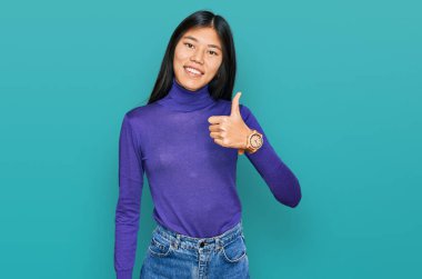 Güzel, genç Asyalı kadın gündelik giysiler giyip mutlu mesut el hareketi yapıyor. Kameraya bakıp başarıyı gösteren ifade. 