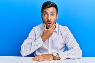 Masada oturan yakışıklı, iş kıyafetleri giyen, elleri çenesinde olan, inançsızlıktan, şaşkınlıktan ve şaşkınlıktan büyülenmiş bir İspanyol. 