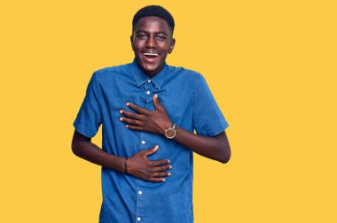 Genç, Afro-Amerikan bir adam, günlük kıyafetler giyiyor, gülümsüyor ve kahkahalarla gülüyor.. 