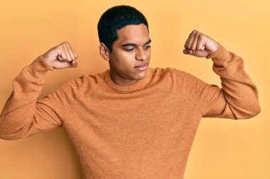 Sıradan bir kazak giyen genç yakışıklı İspanyol gururla gülümseyen kol kaslarını gösteriyor. fitness konsepti. 