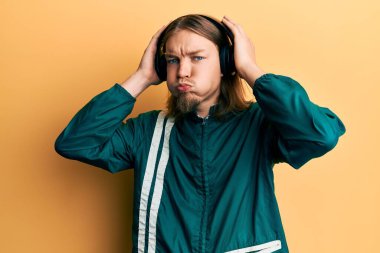 Uzun saçlı, spor kıyafetleri giyen ve kulaklık takan komik suratlı yakışıklı beyaz adam. Ağzı havayla şişer, havayı yakalar.. 