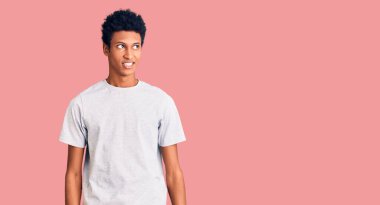 Genç Afro-Amerikan bir adam günlük kıyafetler giyip yüzünde gülümseme, doğal bir ifade ile yan yana bakıyor. Kendinden emin gülen. 