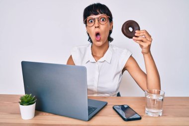 Ofiste çalışan güzel esmer kadın çikolatalı donut yiyor. Korkmuş ve ağzı açık şaşkınlık içinde, inançsız bir yüz. 