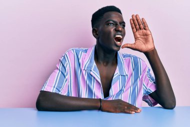 Gündelik giysiler giymiş genç Afro-Amerikalı adam masaya oturmuş el ele tutuşmuş bağırıyor ve çığlık çığlığa bağırıyordu. iletişim konsepti. 