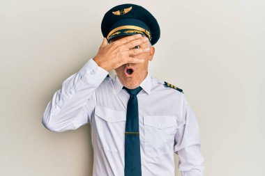 Yakışıklı, orta yaşlı, uçak pilotu üniforması giyen, yüzü ve gözleri kapalı, utangaç ifadesiyle parmaklarından bakan olgun bir adam.. 