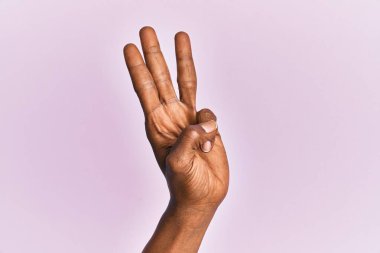 Siyah orta yaşlı kadının kolu ve eli pembe izole edilmiş arka planda. 3 numara üç parmağı gösteriyor. 