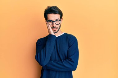 Gündelik kıyafetler ve gözlük takan genç İspanyol adam çapraz kollu depresyondan sıkılmış ve yorgun göründüğünü düşünüyor.. 