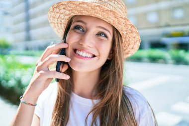 Tatilde gülümseyen genç sarışın kadın şehrin caddesinde akıllı telefondan konuşuyor.