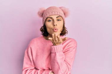 Genç esmer, sevimli yün şapkalı bir kadın kameraya bakıyor ve havada bir öpücük savuruyor. Güzel ve seksi. aşk ifadesi. 