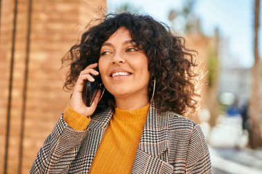 Genç İspanyol iş kadını gülümsüyor. Şehirdeki akıllı telefondan mutlu bir şekilde konuşuyor..