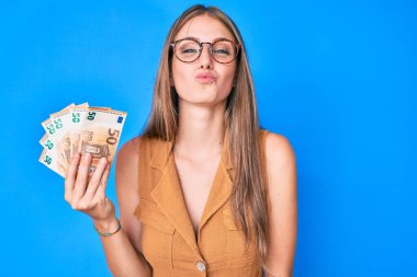 Elinde euro banknotları olan genç sarışın kız, kameraya bakıp öpüşürken çok güzel ve seksi görünüyor. aşk ifadesi. 