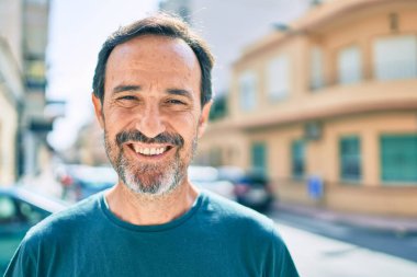 Orta yaşlı, sakallı, açık havada mutlu gülümseyen bir adam.