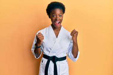 Karate kimonosu ve siyah kuşak giyen Afrikalı genç bir kız kollarını kaldırarak ve açık gözlerle başarıyı kutluyor ve şaşırıyor. Kazanan konsept. 