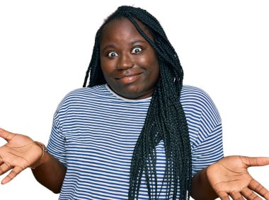 Örgülü, sıradan kıyafetler giyen, elleri ve kolları havada, kafası karışmış genç siyahi bir kadın. şüphe kavramı. 