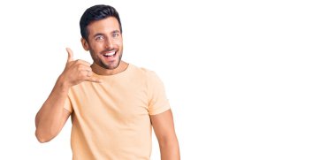 Günlük kıyafetler giymiş, gülümseyen genç İspanyol adam telefonla el ve parmak hareketleri yapıyor telefonda konuşur gibi. iletişim kavramları. 