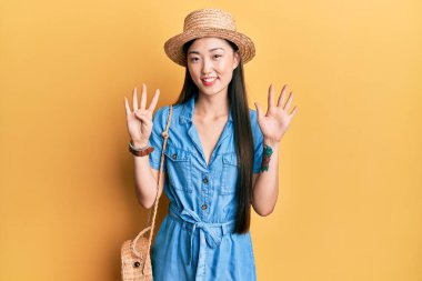 Genç Çinli kadın yaz şapkası takıyor ve dokuz numaralı parmaklarıyla işaret ediyor. Kendinden emin ve mutlu gülümserken.. 