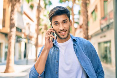 Genç Latin adam gülümsüyor ve şehirde akıllı telefondan konuşuyor..