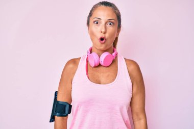 Orta yaşlı İspanyol kadın spor kıyafetleri giyiyor ve kulaklık takıyor. Korkmuş ve ağzı açık bir şekilde şaşırmış, inançsız bir yüz. 