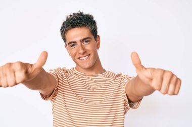 Gündelik giysiler giyen genç bir adam elinle olumlu jest yapıyor, gülümsüyor ve başarı için seviniyor. kazanan jest. 