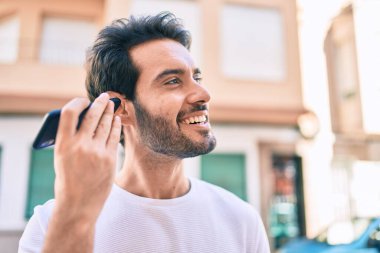 Genç İspanyol adam gülümsüyor. Şehirdeki akıllı telefonu kullanarak mutlu bir sesli mesaj dinliyor..